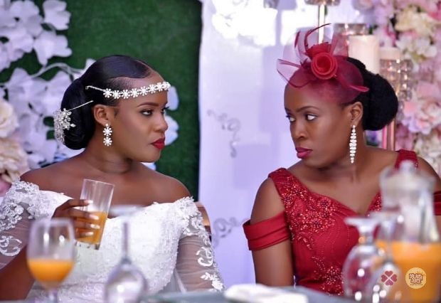 A bride and a guest in red seated together with glasses of fresh juice